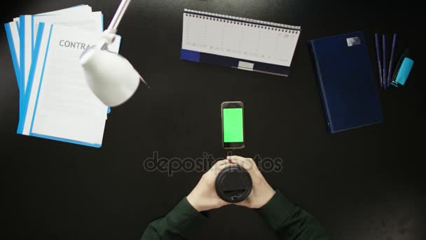 Een man is aan een bureau zitten en met behulp van een telefoon. — Stockvideo