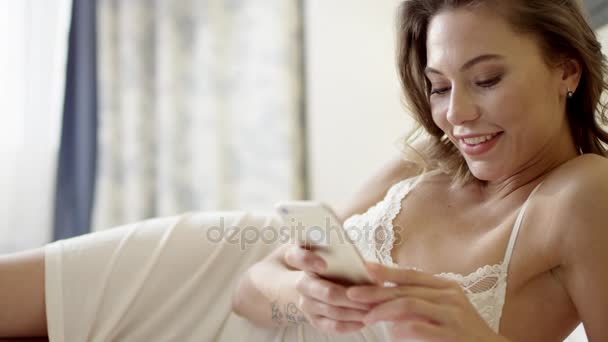 Tender woman lying on bed and using smartphone — Stock Video