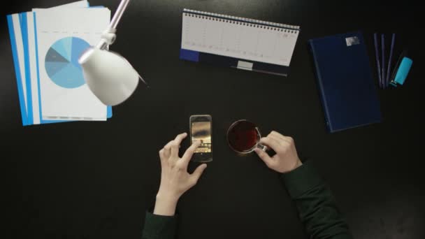 Een man is aan een bureau zitten en met behulp van een telefoon. — Stockvideo