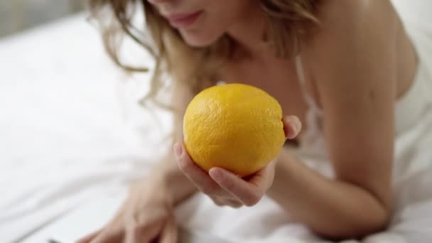 Young woman checking social network on her laptop and holding and orange with grapes on plate near her — Stock Video