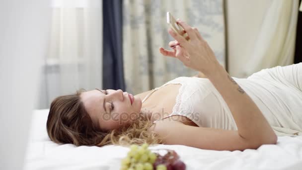 Woman shopping online by using credit card and smartphone while lying on bed — Stock Video