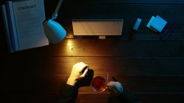 Een man is aan een bureau zitten en met behulp van een telefoon. — Stockvideo