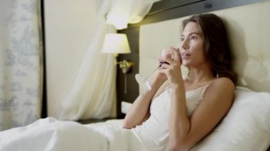 Güzel kadın yatakta yatıyor ve içecekler cam dışında kırmızı şarap smartphone üzerinde konuşurken