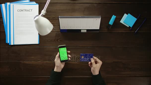 Um homem está sentado em uma mesa de escritório e usando um telefone . — Vídeo de Stock