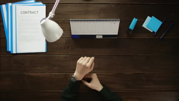 Een man is aan een bureau zitten en met behulp van een telefoon. — Stockvideo