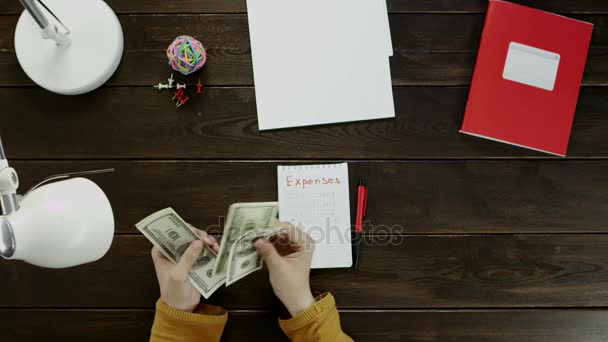 L'homme au bureau colle des autocollants dans le carnet et compte l'argent, à côté du dossier, lampe, boule, bureau et boutons . — Video