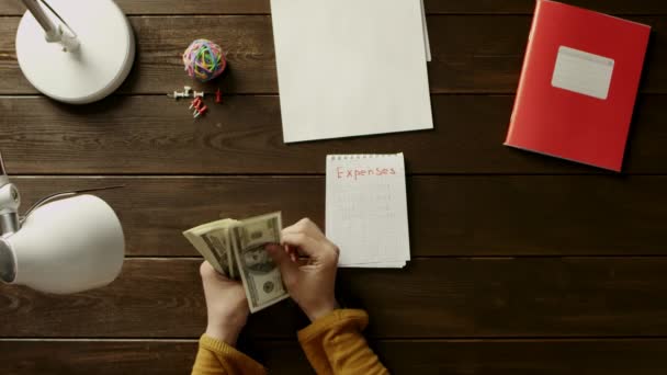 Der Mann am Schreibtisch klebt Sticker in das Notizbuch und zählt Geld, neben Ordner, Lampe, Ball, Büro und Knöpfe. — Stockvideo