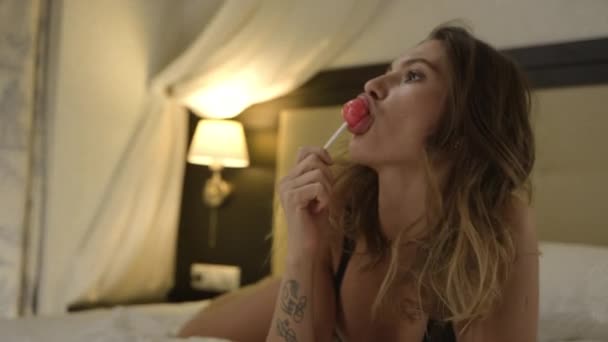 Sexy žena olizuje tvrdé bonbóny na posteli — Stock video