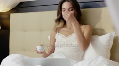 Güzel kadın yatakta kahve yudumlarken bir laptop haber okuma