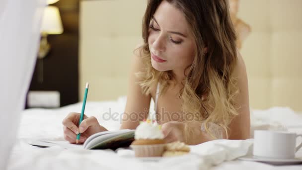 パジャマを着て魅力的な女性が何かを書くのコーヒーとケーキを彼女のノート — ストック動画