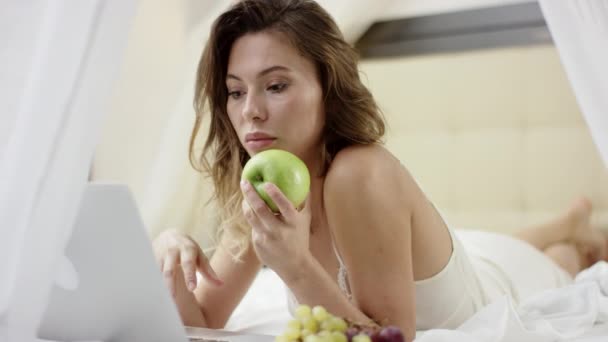 若い女性彼女のラップトップでインターネットをサーフィンし、リンゴを保持 — ストック動画