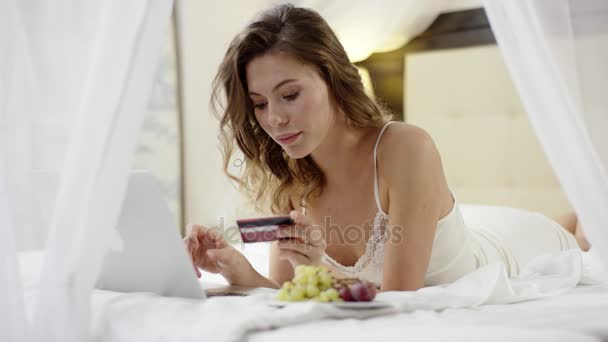 Vrouw ligt op bed en met behulp van haar laptop en creditcard — Stockvideo