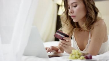 Yatak ve Internet üzerinden bir şey satın almak için onun laptop ve kredi kartı kullanarak üzerinde pijama yalan giyinmiş güzel kadın