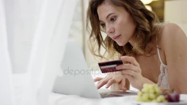 Yatak ve online alışveriş için onun laptop ve kredi kartı kullanarak üzerinde pijama yalan ihale kadın giyinmiş