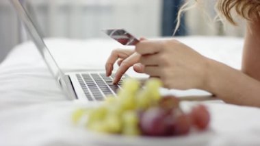 Yatak ve online alışveriş için onun laptop ve kredi kartı kullanarak üzerinde pijama yalan giyinmiş güzel kadın