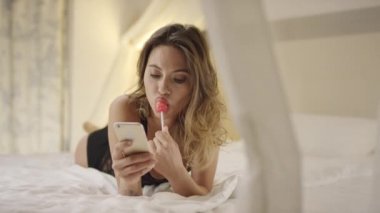 Baştan çıkarıcı kadın manifatura bir smartphone ve yatakta sert şeker yalama