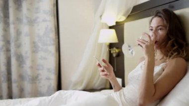 Yatağa beyaz şarap içme sırasında smartphone üzerinde kadın manifatura