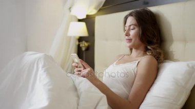 Yatakta akıllı telefon kullanan kadın.