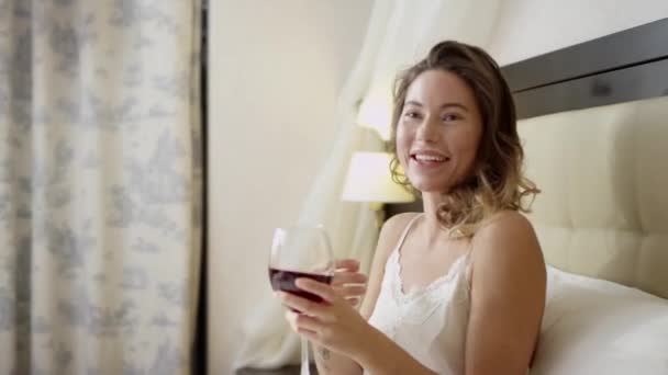 Young woman drinks red wine on bed — Stock Video