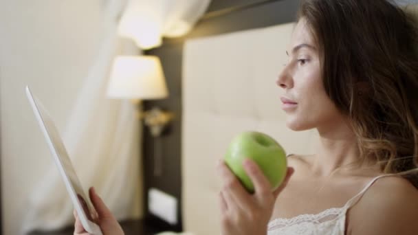 Kvinna med TabletPC och ett äpple i sängen — Stockvideo