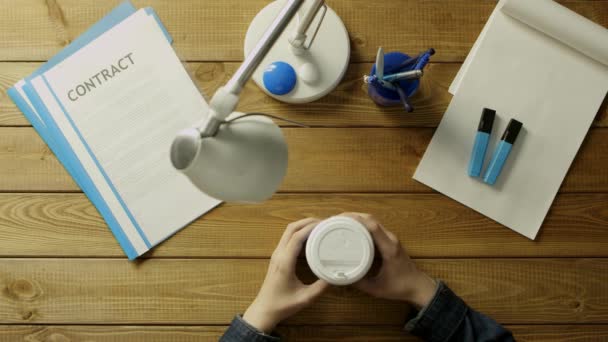 Мужчина сидит за рабочим столом в телефоне и пьет кофе. На письменном столе канцтовары в сине-белых тонах . — стоковое видео
