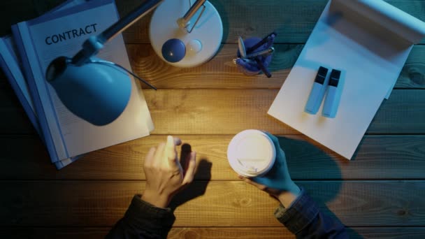 Un hombre está sentado en el escritorio de la oficina en el teléfono y beber café. Sobre el escritorio suministros de oficina en tonos azules y blancos . — Vídeos de Stock