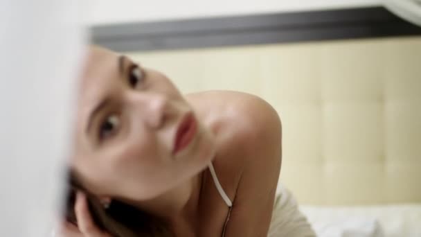 Сексуальная женщина в белом нижнем белье с капюшоном, демонстрирующая свое подтянутое тело и страстно смотрящая на камеру в спальне — стоковое видео