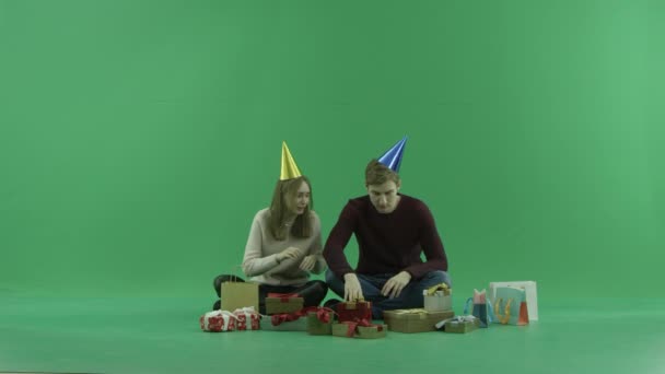 Νεαρό ζευγάρι κάθεται μεταξύ χριστουγεννιάτικα δώρα και τσάντες και προσπαθεί να επιλέξει ένα, chroma κλειδί στο φόντο — Αρχείο Βίντεο
