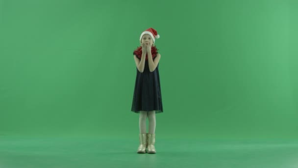 Милая маленькая девочка в рождественской шляпе посылает воздушные поцелуи, хрома ключ на заднем плане — стоковое видео