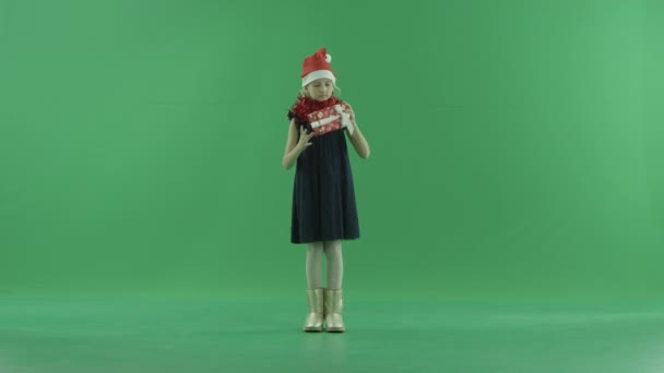 Roztomilá holčička v Christmas hat se snaží pochopit, co se skrývá ve vánoční krabičce, klíčování chroma na pozadí — Stock video