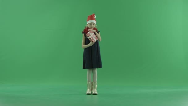 Adorable little girl in Christmas hat tries to realise what lies in Xmas present box, chroma key on background — Stock Video