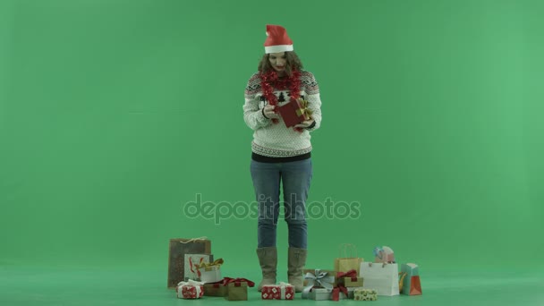 Affascinante giovane donna in cappello di Natale cercando di realizzare ciò che si trova nella sua scatola regalo di Natale, chiave cromatica sullo sfondo — Video Stock