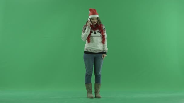 Jeune femme excitée en chapeau de Noël parlant sur son smartphone tandis que se tient debout, clé chromatique sur fond — Video