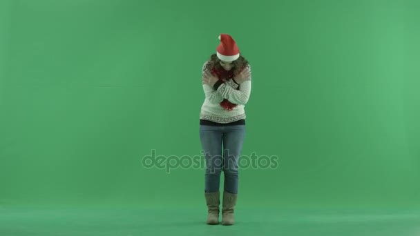 Zavallı genç kadın chroma anahtar arka plan üzerinde Noel şapka donuyor ve sıcak, tutmak için çalışıyor — Stok video