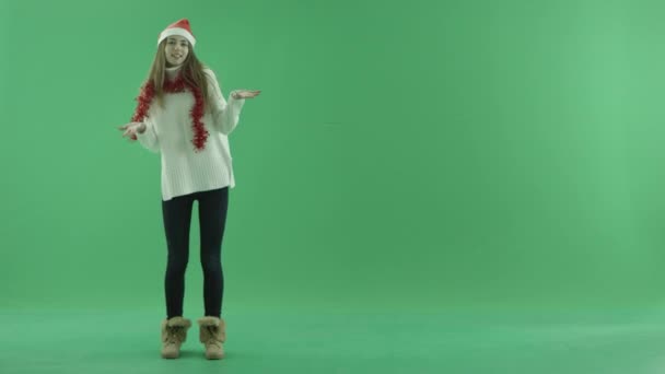 Encantadora jovem beleza no chapéu de Natal mostra algo perto dela e conta sobre isso, chave chroma no fundo — Vídeo de Stock