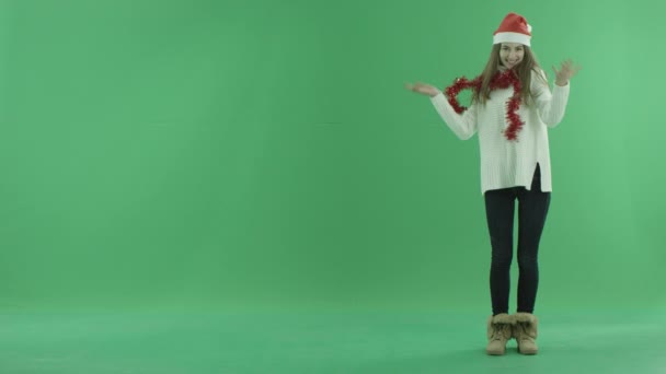 Preciosa hembra en sombrero de Navidad muestra algo cerca de ella y cuenta sobre ella, croma clave en el fondo — Vídeo de stock