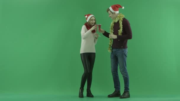 Jovem casal feliz bebe vinho tinto e sopra para apito de Natal com chave chroma no fundo — Vídeo de Stock