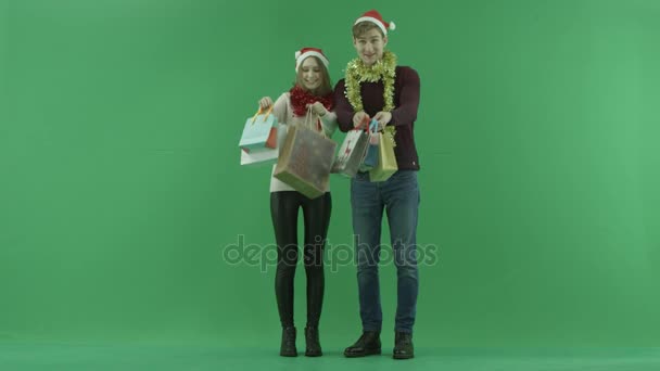 Mladý pár ukazuje jejich nákupní tašky k fotoaparátu, chroma key, na pozadí — Stock video