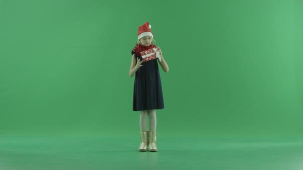 Carino bambina in cappello di Natale cerca di capire cosa si trova nella scatola regalo di Natale, chiave cromatica su sfondo — Video Stock