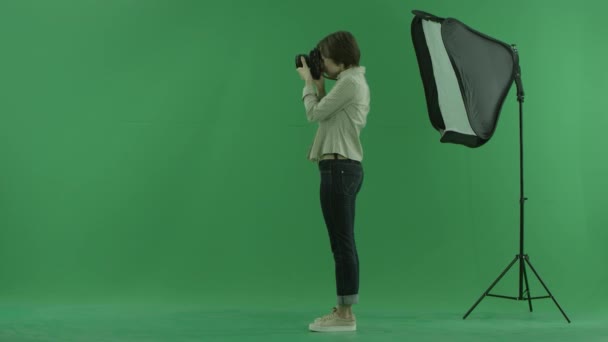 Молодая женщина фотографирует слева на зеленом экране и исправляет положение модели — стоковое видео