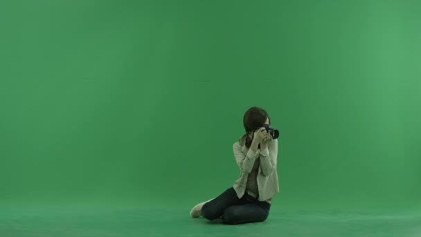 Sittande ung kvinna tar foton runt henne på grön skärm — Stockvideo