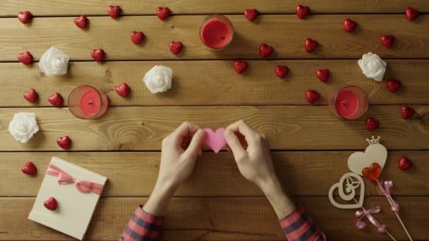Vrolijke man met handgemaakte hart van papier zit door tabel, bovenaanzicht — Stockvideo