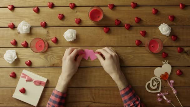 Jonge man met handgeschept papier hart zit door houten tafel, bovenaanzicht — Stockvideo