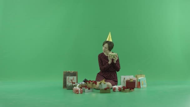 Μια νεαρή γυναίκα κάθονται και τίναγμα κουτιά δώρων γύρω της σχετικά με την πράσινη οθόνη — Αρχείο Βίντεο