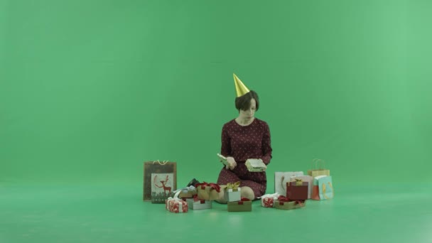Eine junge Frau sitzt auf dem grünen Bildschirm und öffnet leere Geschenkboxen um sie herum. — Stockvideo