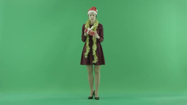 Una mujer joven está buscando un regalo de Navidad y sacudiéndolo en la pantalla verde — Vídeo de stock