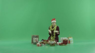 Genç bir kadın oturuyor ve onun etrafında yeşil ekranda boş Noel hediyeleri açma