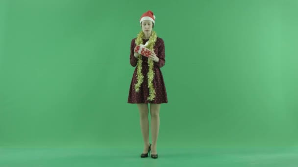 A young woman is looking for a Christmas gift and shaking it on the green screen — Stock Video