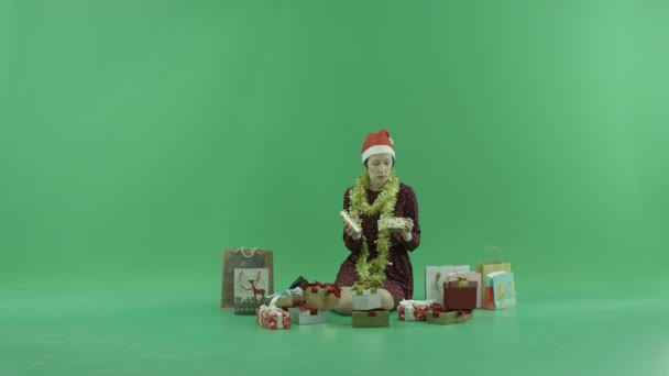若い女性が座っていると緑色の画面に彼女の周りの空のクリスマス プレゼントを開く — ストック動画