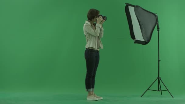 Молодая женщина фотографирует справа на зеленом экране и исправляет положение модели — стоковое видео